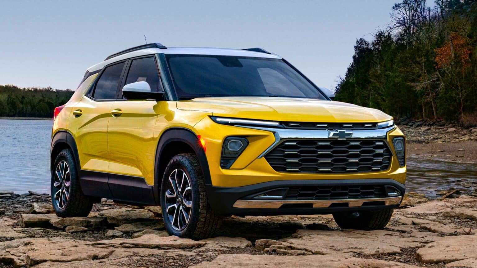 Chevrolet SUV parked beside a river on rocky terrain, showcasing a vibrant yellow exterior, modern design elements, and distinctive front grille. Ideal for outdoor adventures and versatile driving experiences.