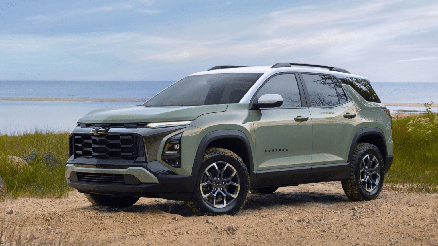Chevrolet Equinox SUV parked on sandy terrain near a beach, showcasing a sleek green exterior and modern design with rugged tires, emphasizing its versatility for outdoor adventures.