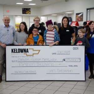 Group photo of community members and representatives presenting a large check for $5,000 to a local charitable organization at a Kelowna dealership event.