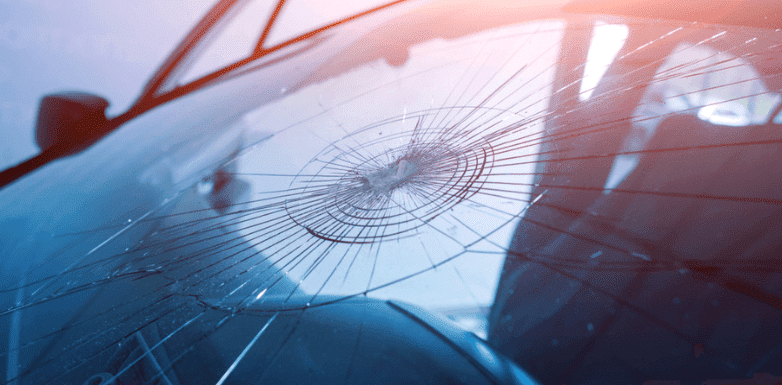 Close-up of a cracked car windshield with spiderweb-like fractures radiating from a central impact point, highlighting the need for auto glass repair services.