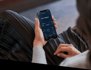 A close-up of a person's hand holding a smartphone displaying a modern mobile app interface, with sleek design elements, on a cozy setting featuring a soft gray sweater and a striped skirt.