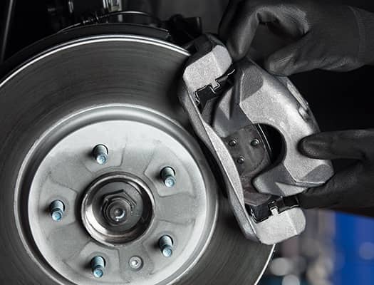 Close-up of a mechanic's hands installing a new brake caliper onto a car's brake rotor, highlighting the components used in vehicle braking systems.