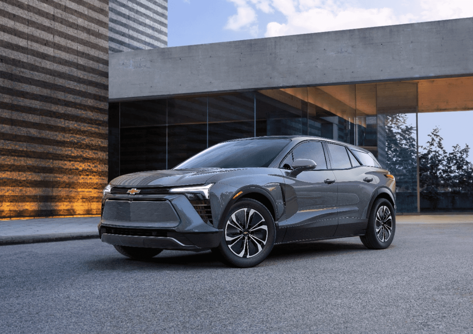 Modern Chevy electric SUV parked in front of a contemporary building, showcasing sleek lines and innovative design. The vehicle stands out with its aerodynamic shape and stylish wheels, emphasizing its advanced technology and eco-friendly features.