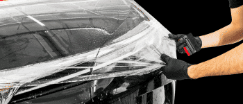 Close-up of a technician applying protective film to a vehicle's hood, demonstrating a paint protection film installation process to shield the car’s surface from scratches and damage.