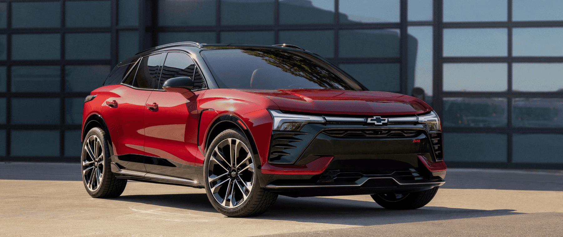 Sleek red Chevrolet SUV parked in front of a modern glass building, showcasing bold design features, sporty wheels, and a striking front grille suitable for urban driving and outdoor adventures.
