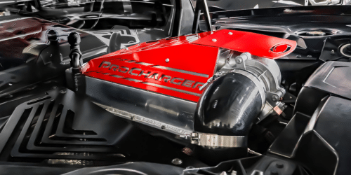 High-performance ProCharger supercharger installed on a car engine, showcasing its distinctive red casing and sleek design amidst the engine bay components.