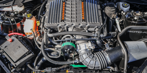 Close-up view of a high-performance Magnuson supercharger in an automotive engine bay. The image showcases the supercharger, intake system, and surrounding components, highlighting advanced automotive engineering and performance upgrades.