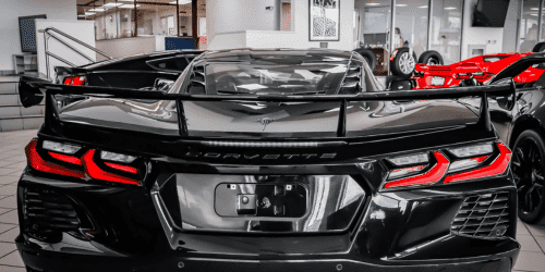 Rear view of a black Chevrolet Corvette showcasing its sleek design, prominent rear wing, and distinctive taillights, displayed in a luxury car dealership.