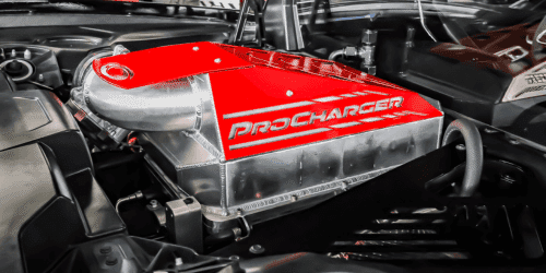 Close-up view of a ProCharger supercharger installed in a high-performance engine bay, showcasing its sleek red design and polished aluminum housing.