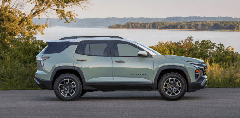 Side view of a modern SUV parked along a scenic lakeside, showcasing its sleek design, contemporary body color, and all-terrain tires, surrounded by greenery and a tranquil landscape in the background.