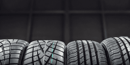 Close-up image of a modern car wheel featuring a stylish multi-spoke design in black and silver, mounted on a performance tire. The backdrop showcases a vibrant and colorful environment, emphasizing the vehicle's sporty aesthetic.